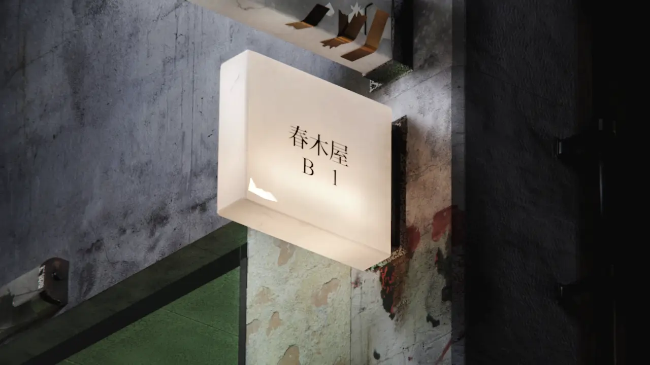 An illuminated sign box mounted on a dark concrete wall, Japanese lettering glowing on its face