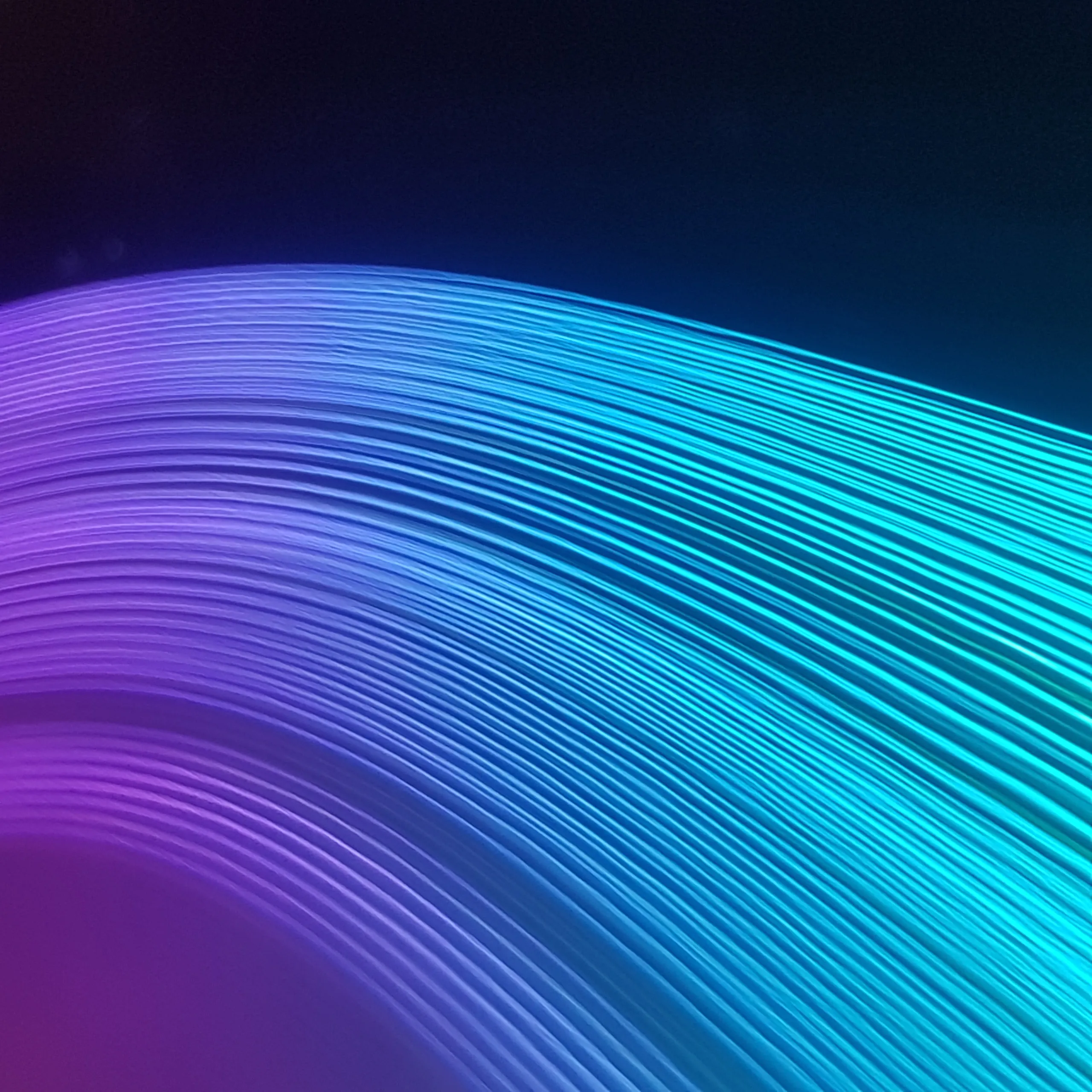 Long-exposure light painting — a fan of fine parallel light trails sweeping across black, graded from violet at the left to cyan at the right