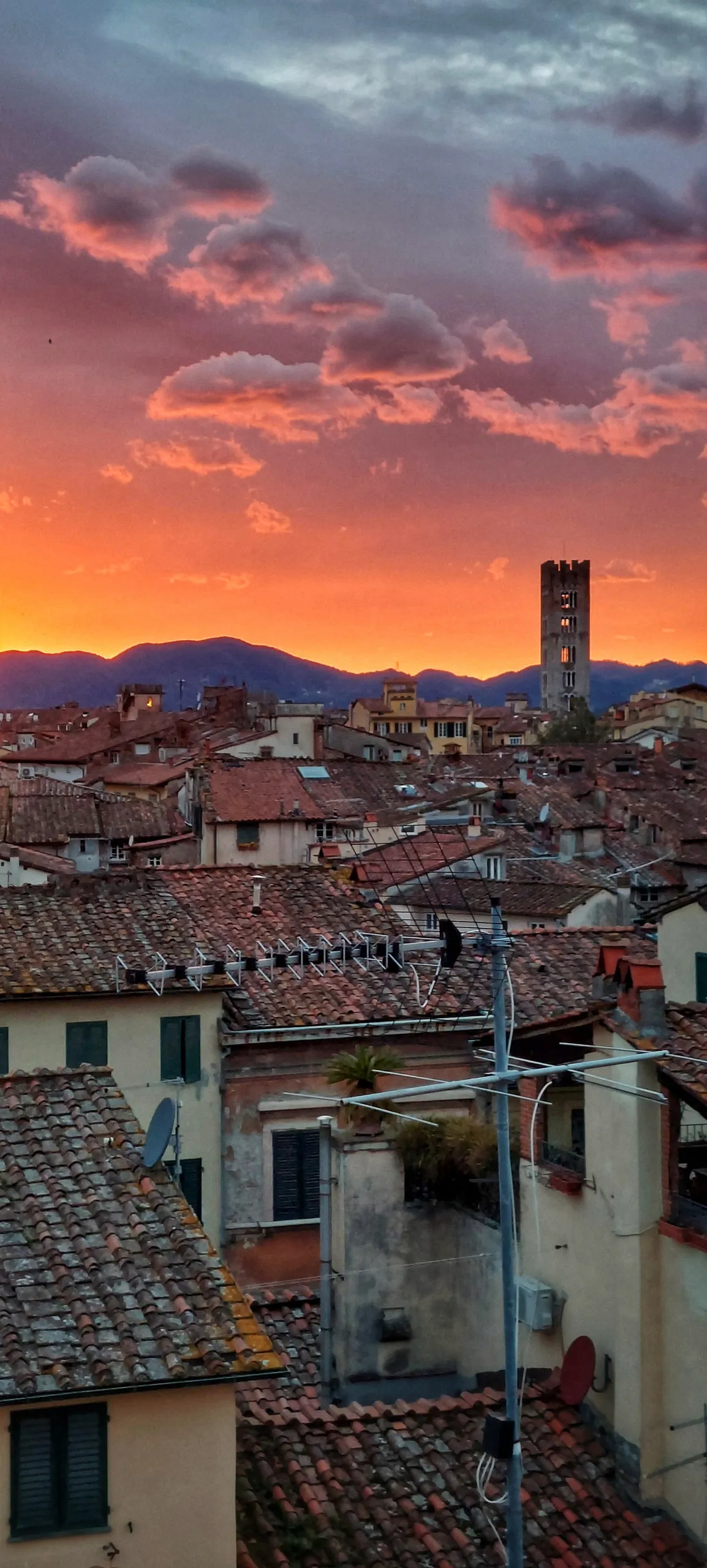 Terracotta rooftops of an Italian hill town at sunset, a stone bell tower against an orange sky
