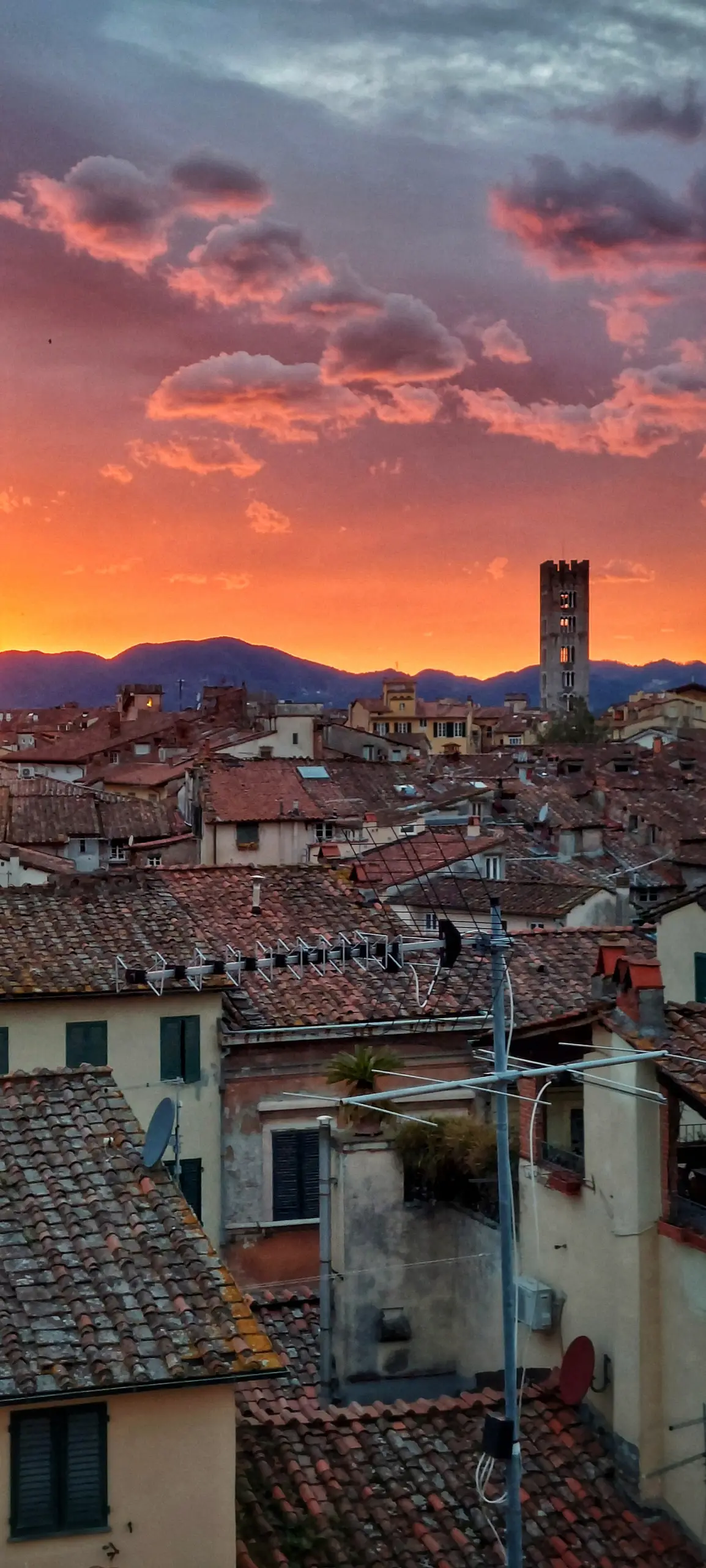 Terracotta rooftops of an Italian hill town at sunset, a stone bell tower against an orange sky