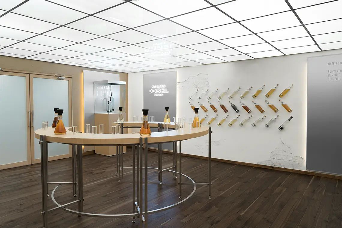 Curved tasting counter with decanters and tall glasses, bottles mounted diagonally along a white wall behind it