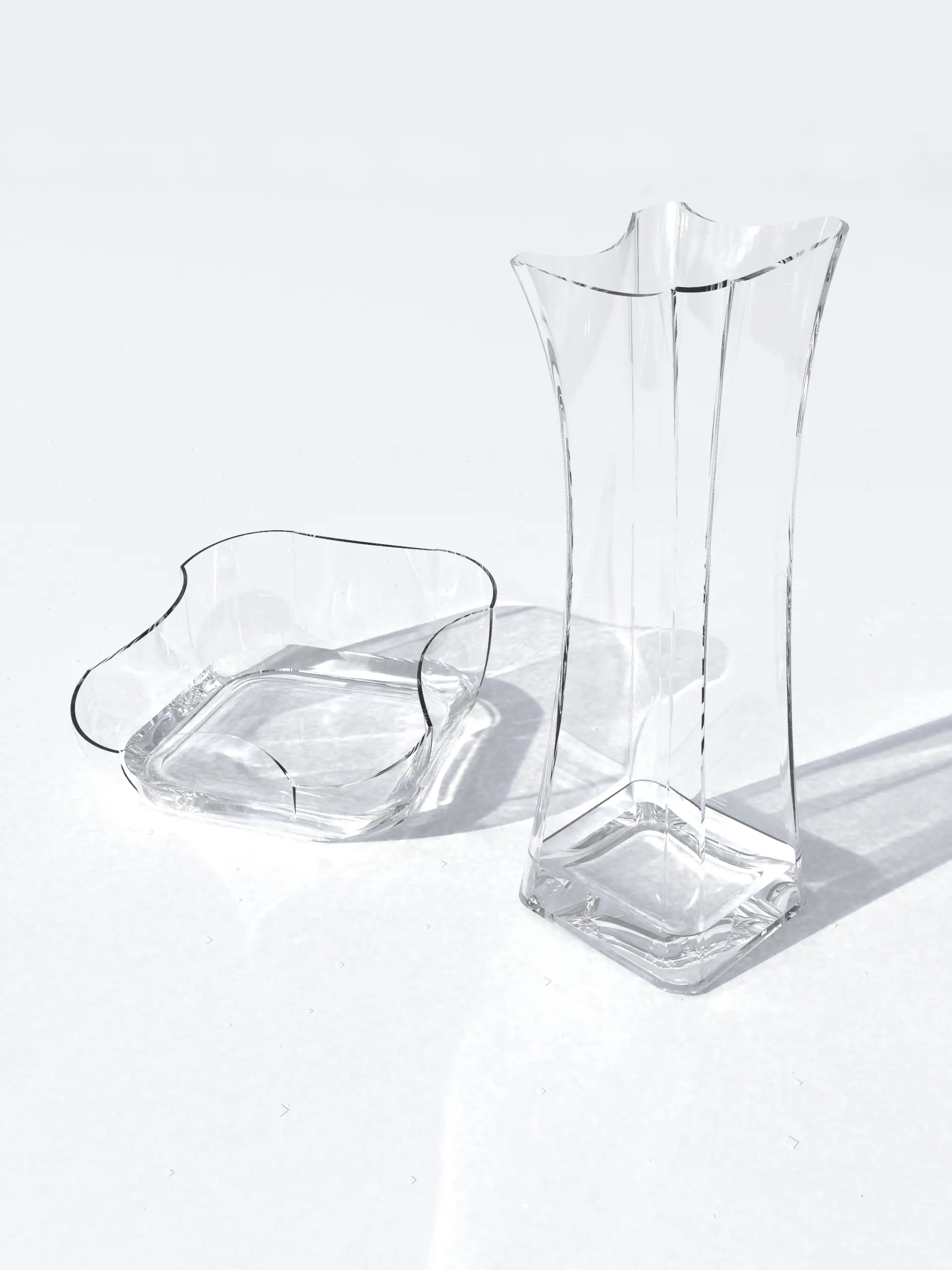 A tall faceted glass vase and a wavy-rimmed glass bowl on white