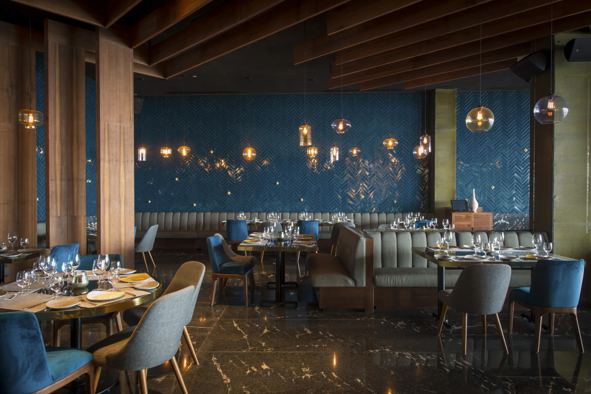 Restaurant interior with deep blue banquettes, brass pendants and a mural wall