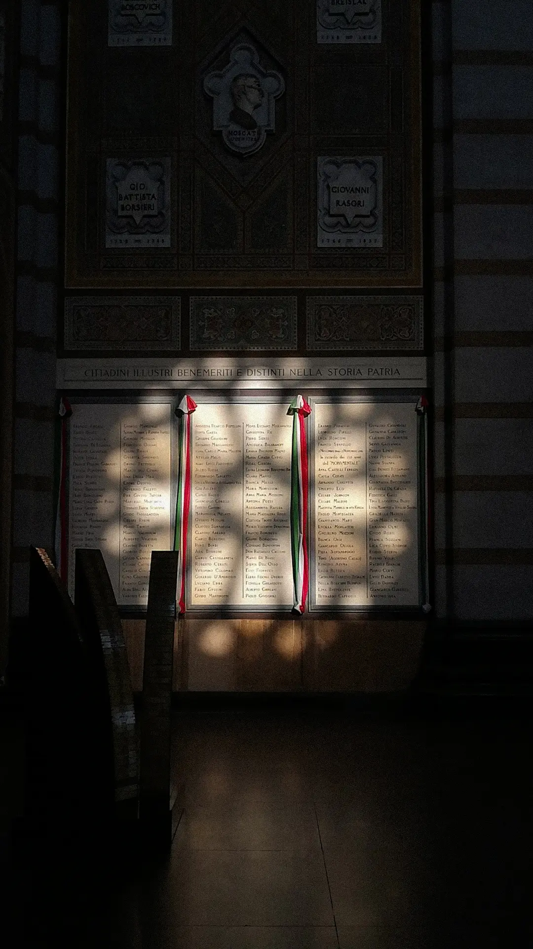 Dappled window light falling across an interior wall hung with framed prints