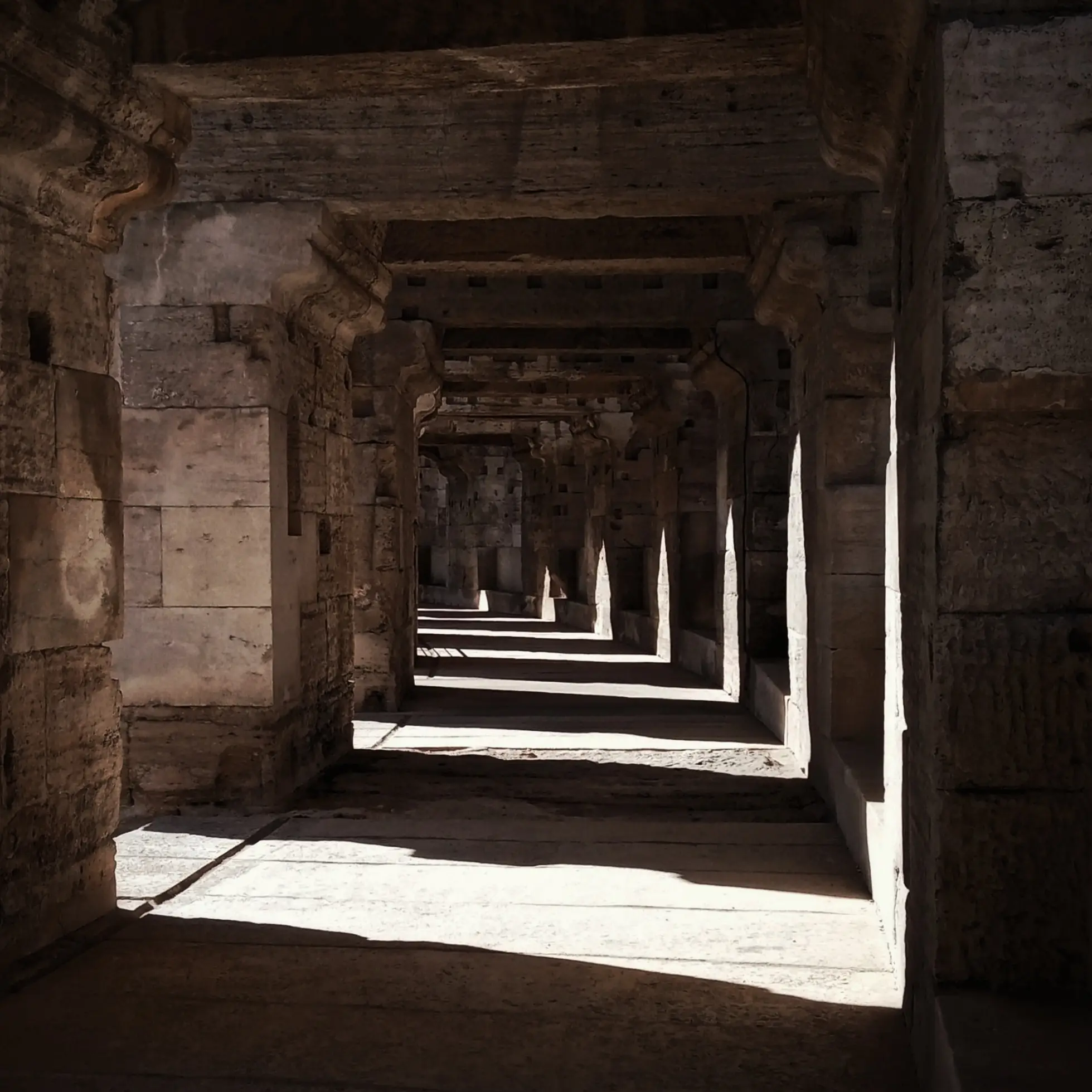 Stone colonnade receding into shadow, raking light striking each successive pier