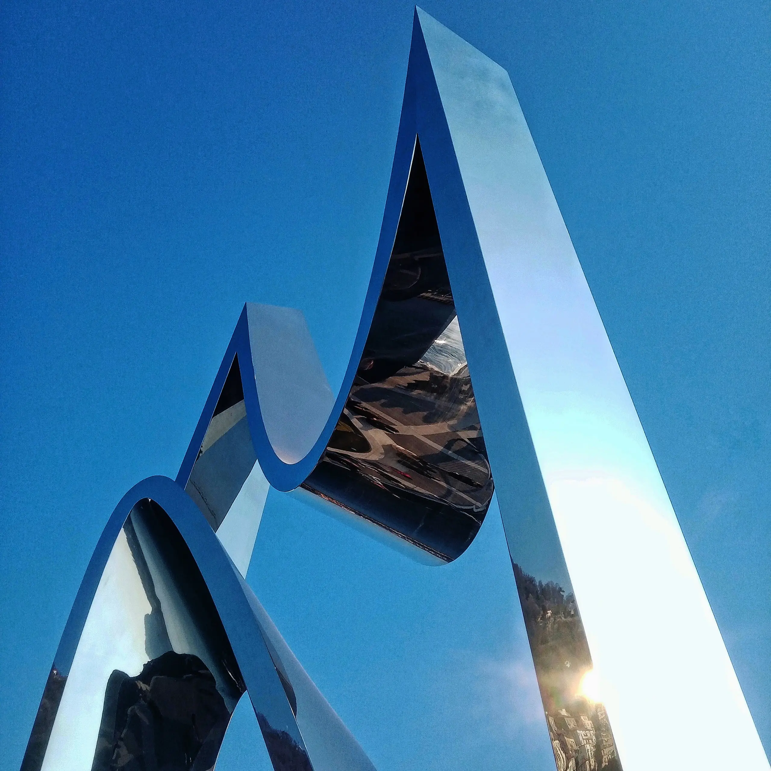 Looking up at a polished stainless steel sculpture, its folded planes mirroring the blue sky