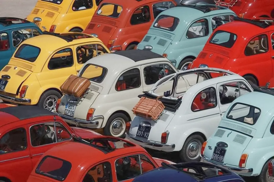 A field of classic Fiat 500s parked nose to tail — the same body in yellow, red, cream, mint and blue