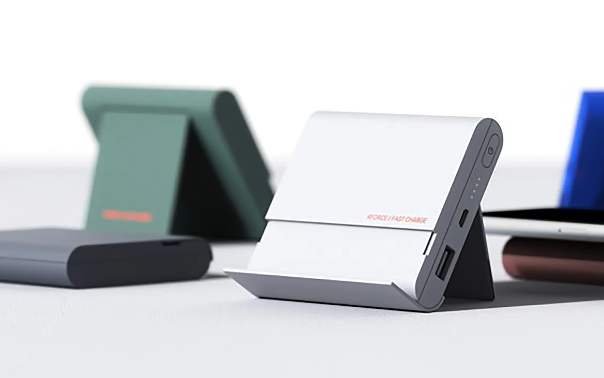 A family of folding power banks propped open like easels — white in the foreground, sage green and blue behind