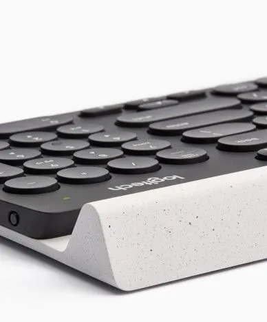 Corner of a Logitech keyboard with round keys, resting in a speckled white concrete cradle