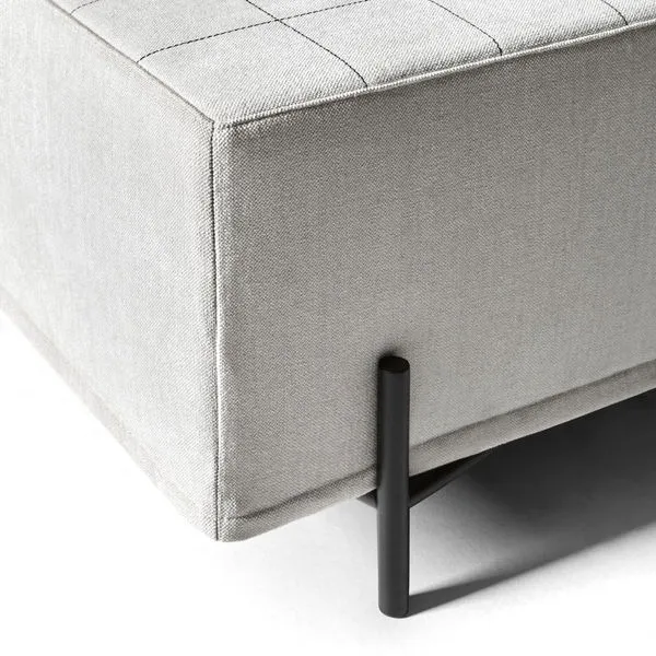 Macro of a white pouf's corner — the quilted grid of the upholstery running into a thin black steel foot
