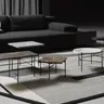 A low, dark living room — a black sofa behind a cluster of Paesaggi Sospesi tables at three heights, stone tops on thin black legs, on a pale striped rug