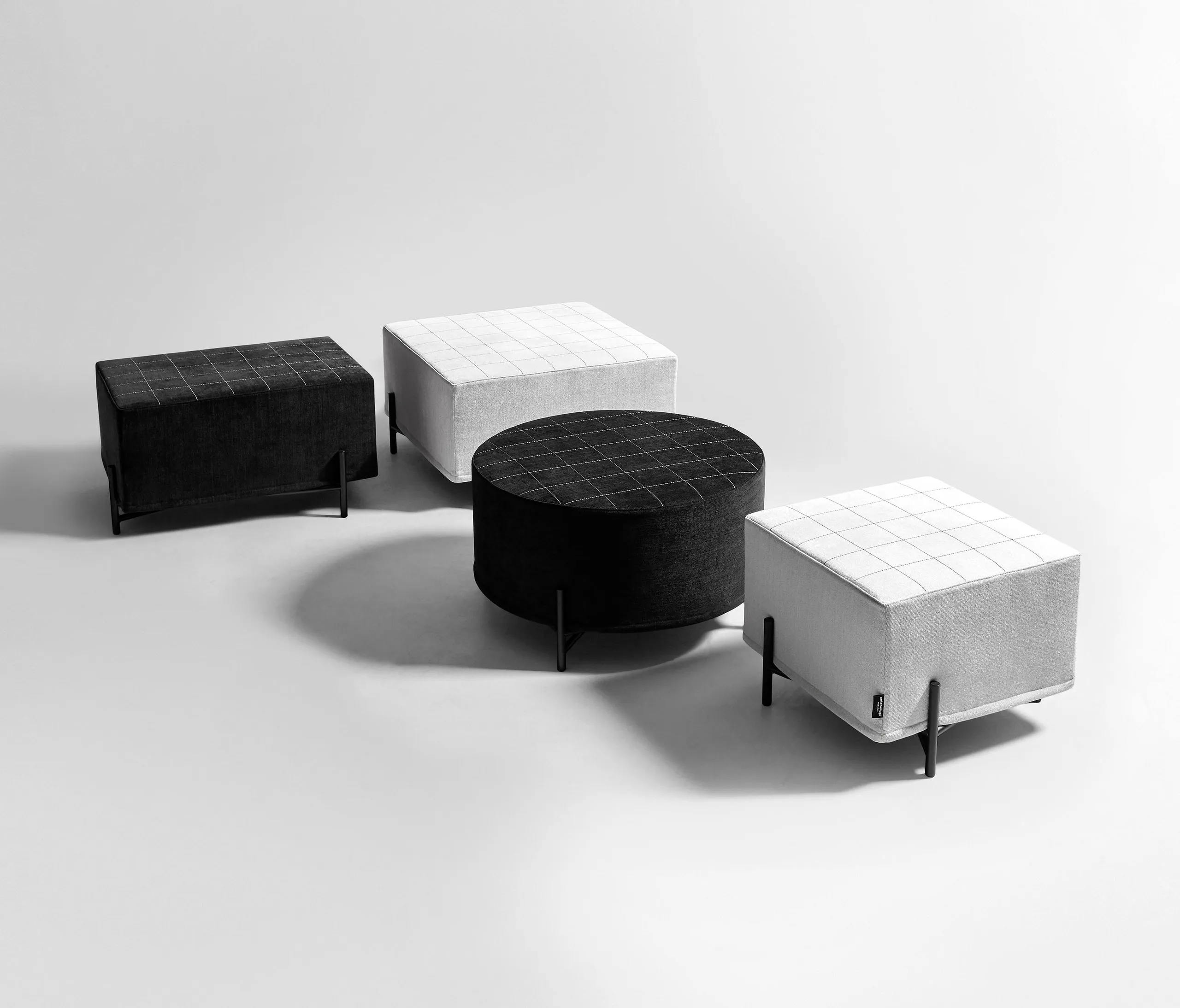 The pouf family on white — quilted black and white upholstery, round and rectangular, on the same thin black legs