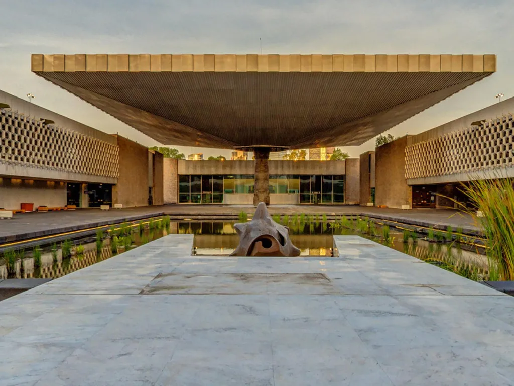 The courtyard of the Museo Nacional de Antropología across its reflecting pool — the vast flat canopy of El Paraguas carried on a single column, the museum's lattice façades either side