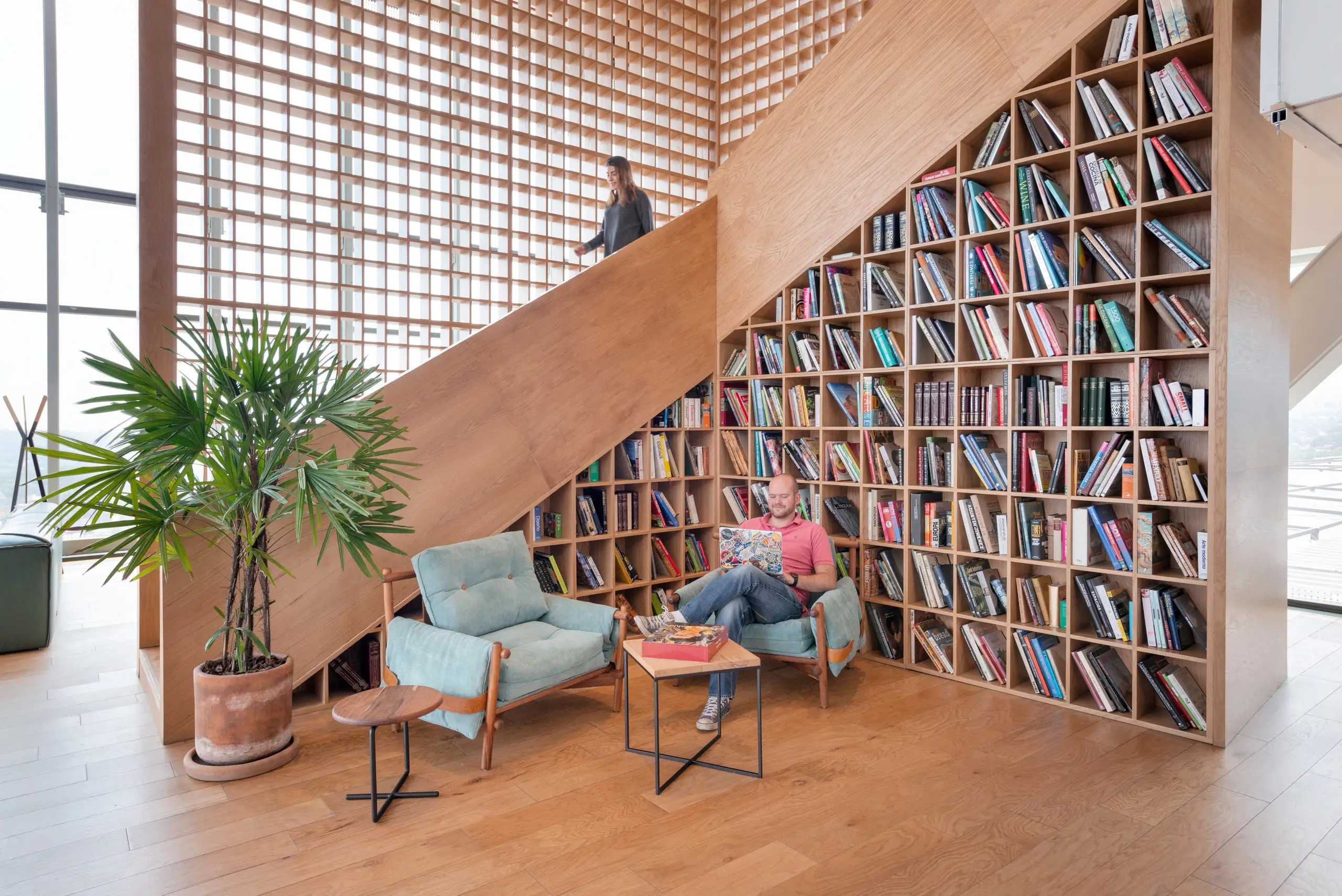 Office lounge beneath a full-height shelving wall filled with colour-sorted books